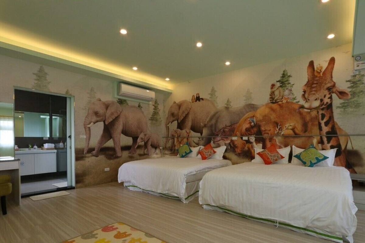 Habitación de hotel con dos camas, un espejo y un mural de elefantes y jirafas.
