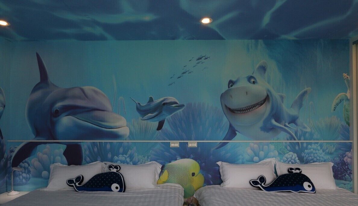 A room with a mural of marine life, including dolphins and a shark, and two beds with whale-shaped pillows.