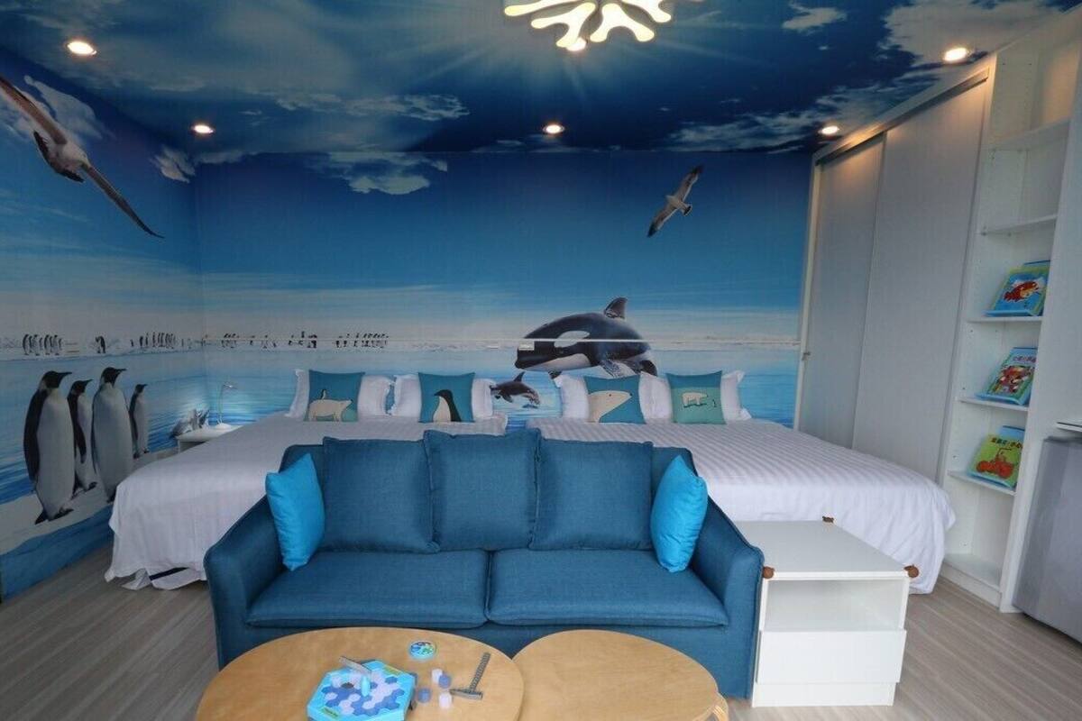Habitación con un mural de una playa, una cama, un sofá azul y una pequeña mesa con juguetes.