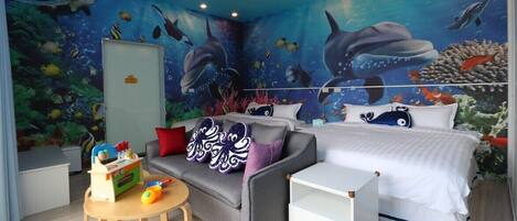Una habitación con un mural submarino, una cama, un sofá, una mesita y un mueble de almacenamiento.