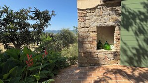 Un mur de pierres avec une porte verte et deux bouteilles vertes sur une terrasse en briques.