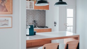A modern kitchen with a white countertop, wooden cabinets, and a gas stove. There are two chairs with cushions and a hanging light fixture above the counter. - Bright two-room apartment just minutes from the historic center (Reggio Emilia)