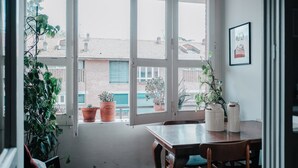 A room with a large window, a wooden table, and potted plants. - Bright two-room apartment just minutes from the historic center (Reggio Emilia)