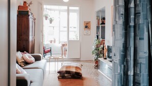 A cozy living room with a sofa, a small table, and a TV stand. There is a door leading to an outdoor area with plants. - Bright two-room apartment just minutes from the historic center (Reggio Emilia)