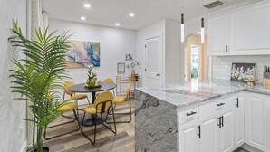 Cocina moderna con armarios blancos, encimera de granito y comedor con sillas amarillas.