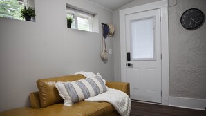 Une pièce avec un canapé en cuir marron, une porte blanche, une horloge au mur et une fenêtre avec des stores.