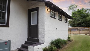Une maison à l’extérieur blanc, avec une porte sombre et un petit escalier menant à l’entrée.