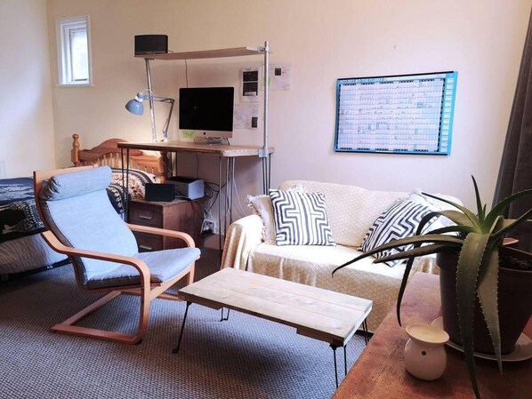A furnished living room with a desk, a computer, a chair, a sofa, and a potted plant.