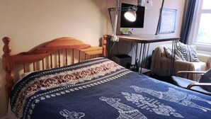 A hotel room with a wooden bed, a desk with a computer, a chair, and a window with curtains. - Cosy 1 Bed Flat Hideout in North London (London)