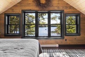 A bedroom with a large window, a bed, and a checkered rug. - Four-Season Luxury Lakefront Cabin Close to Camden and Rockland (Hope)