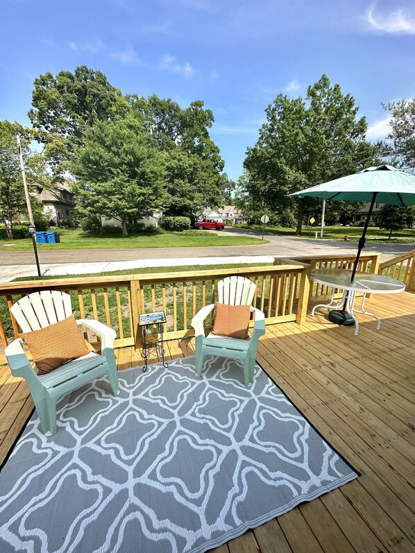 A deck with two Adirondack chairs, a table, and a patterned rug.