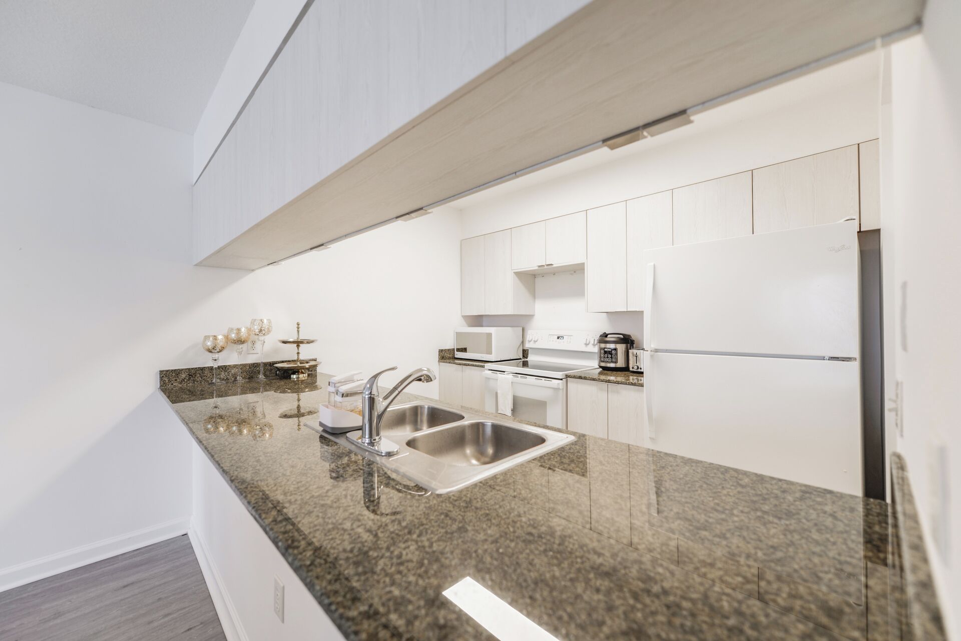 Una cocina moderna con armarios blancos, encimeras de granito y electrodomésticos de acero inoxidable, incluyendo un horno empotrado.