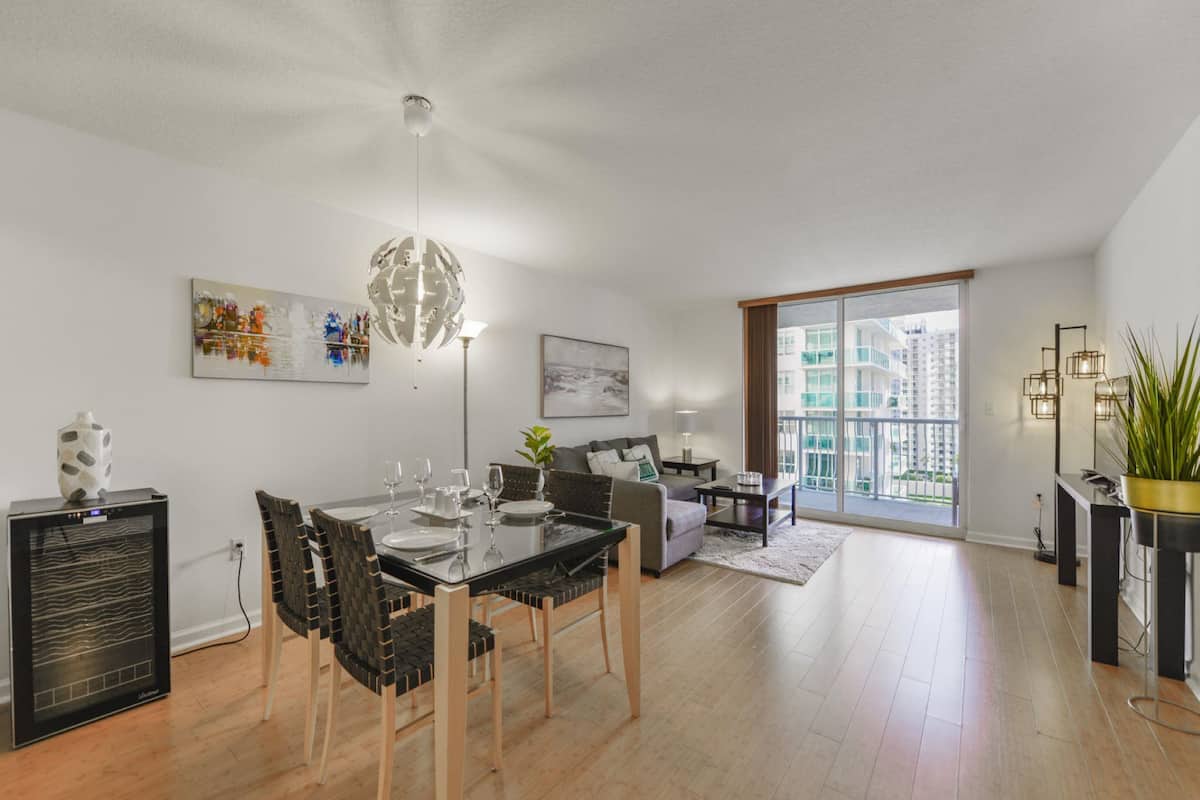 A modern living room with a dining area, a sofa, a coffee table, and a large window with a view of buildings.