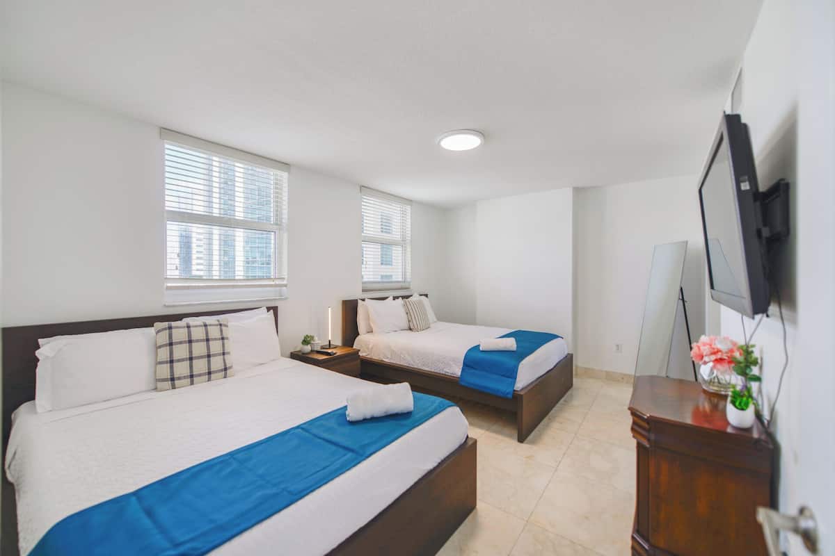 A hotel room with two beds, a TV, and a desk with a plant.
