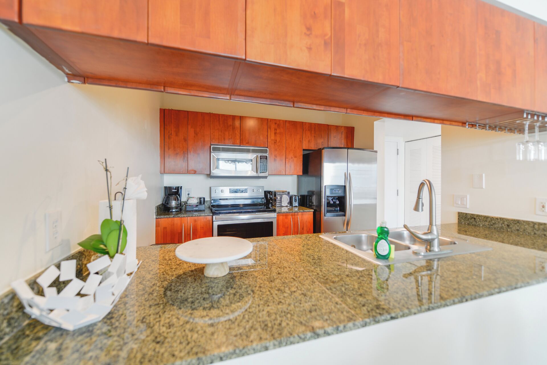 A modern kitchen with wooden cabinets, stainless steel appliances, granite countertops, and a built-in oven.