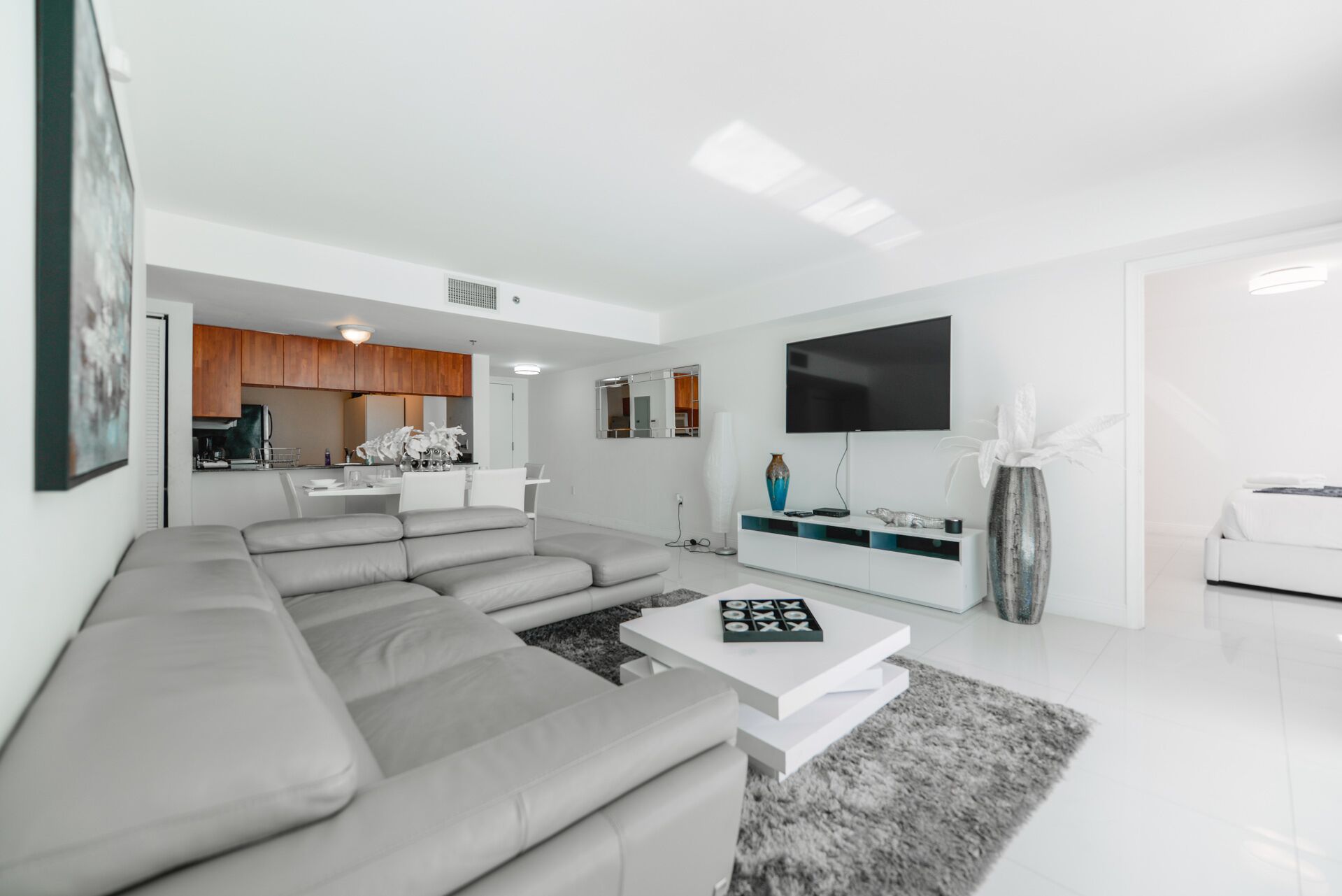 A modern living room with a grey sectional sofa, a white coffee table, and a flat-screen TV mounted on the wall.