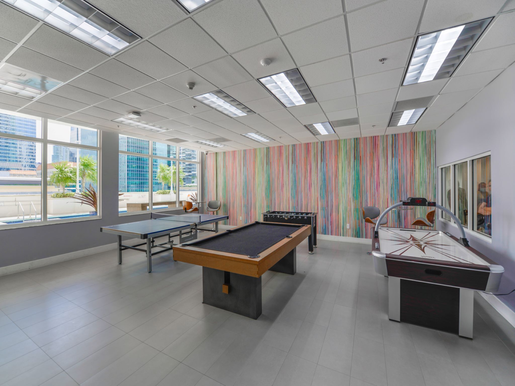 A modern indoor recreational area with a pool table, foosball table, and ping pong table.