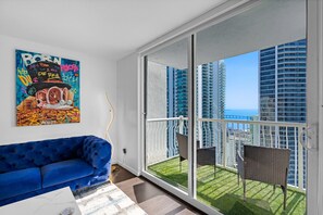 A modern living room with a blue sofa, a glass door leading to a balcony with a view of high-rise buildings and the ocean. - The Club at Brickell Bay (Miami)