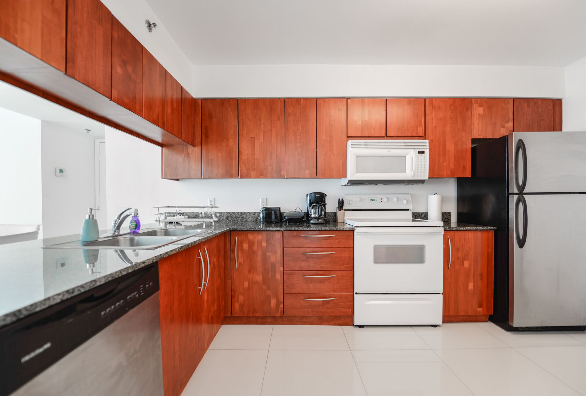 Eine moderne Küche mit Holzschränken, einem Edelstahlkühlschrank, einem weißen Backofen, einer Mikrowelle und einem Geschirrspüler.