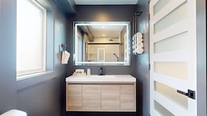 Un baño moderno con un espejo grande, un lavabo blanco y un tocador de madera.