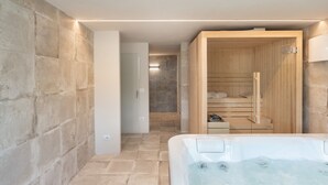 A modern bathroom with a stone wall, a wooden sauna, and a bathtub.