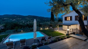 A pool area with lounge chairs and an umbrella, surrounded by a wooden deck and a view of a hillside.