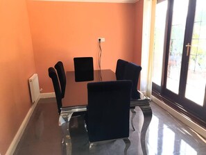 A conference room with a glass table, four black chairs, a black screen on the wall, and a radiator on the left. - Lovely 4-bed , 3 Bath Villa in Bolton, Manchester (Bolton)