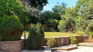 A stone patio with steps leading to a brick wall, surrounded by various shrubs and trees. - Lovely 4-bed , 3 Bath Villa in Bolton, Manchester (Bolton)