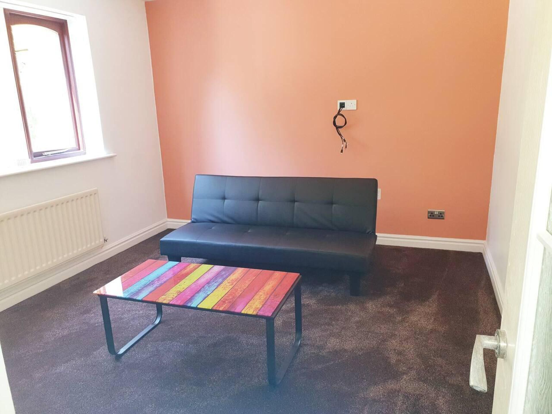 A room with a dark sofa, a colorful striped table, and a radiator.