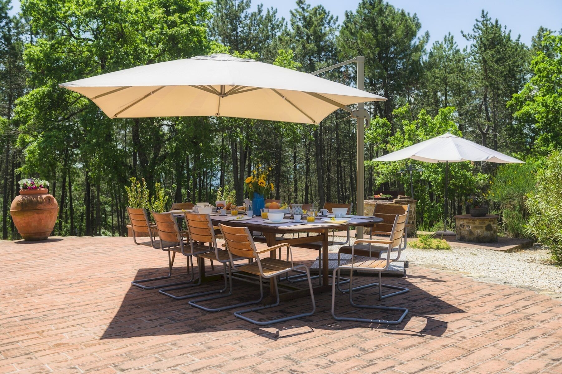 Eine Terrasse im Freien mit einem runden Tisch, Stühlen, zwei großen Sonnenschirmen und einem Blumentopf.