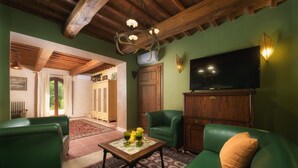 A cozy living room with green leather sofas, a wooden cabinet, and a television. - Podere Santa Croce 10, Emma Villas (Radicondoli)