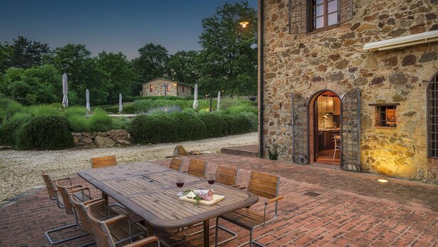 A stone building with a dining area featuring a wooden table and chairs, surrounded by a gravel path and greenery. - Podere Santa Croce 10, Emma Villas (Radicondoli)