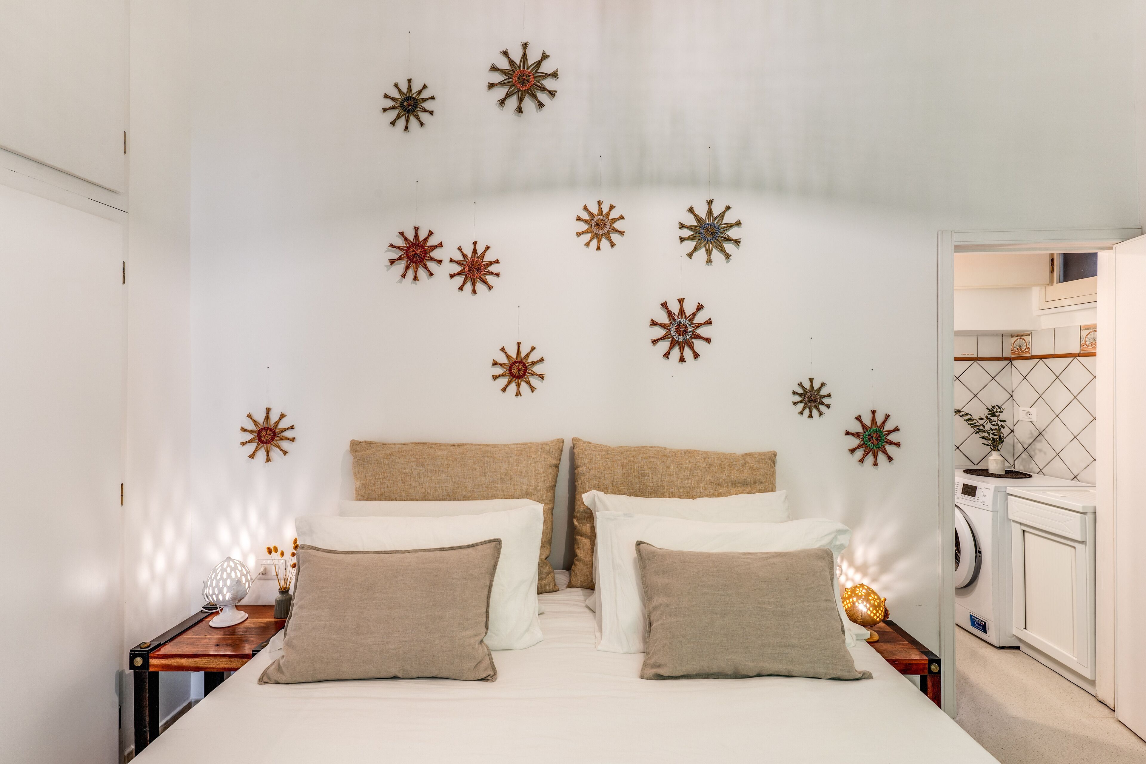 A bedroom with a bed, pillows, a nightstand, a wall-mounted star decoration, and a washing machine in the corner.