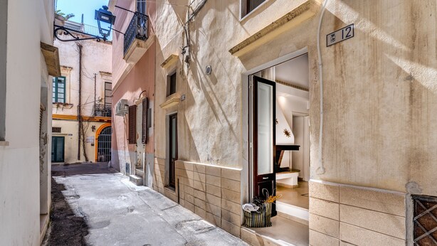 A narrow alleyway with a building on the right featuring a tiled facade and a door with a window. - U Quardianu - Le Case di Valentina (Gallipoli)