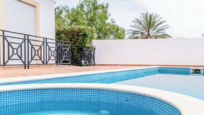 Una piscina con borde de azulejos, cerca metálica y pared blanca al fondo.