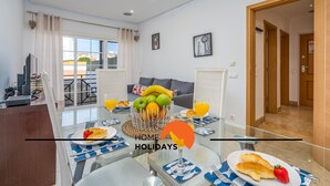 Una sala de estar moderna con una mesa de vidrio dispuesta para el desayuno, un sofá y vistas al balcón.