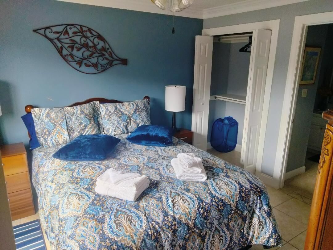 A bedroom with a patterned bedspread, two pillows, a bedside lamp, and a door leading to another room.