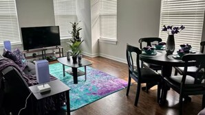 Een woonkamer met een flatscreen televisie, een salontafel, een bank en een eethoek met een tafel en stoelen.