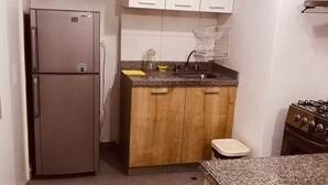 Een kleine keuken met een koelkast, houten kastjes, een spoelbak en een fornuis.