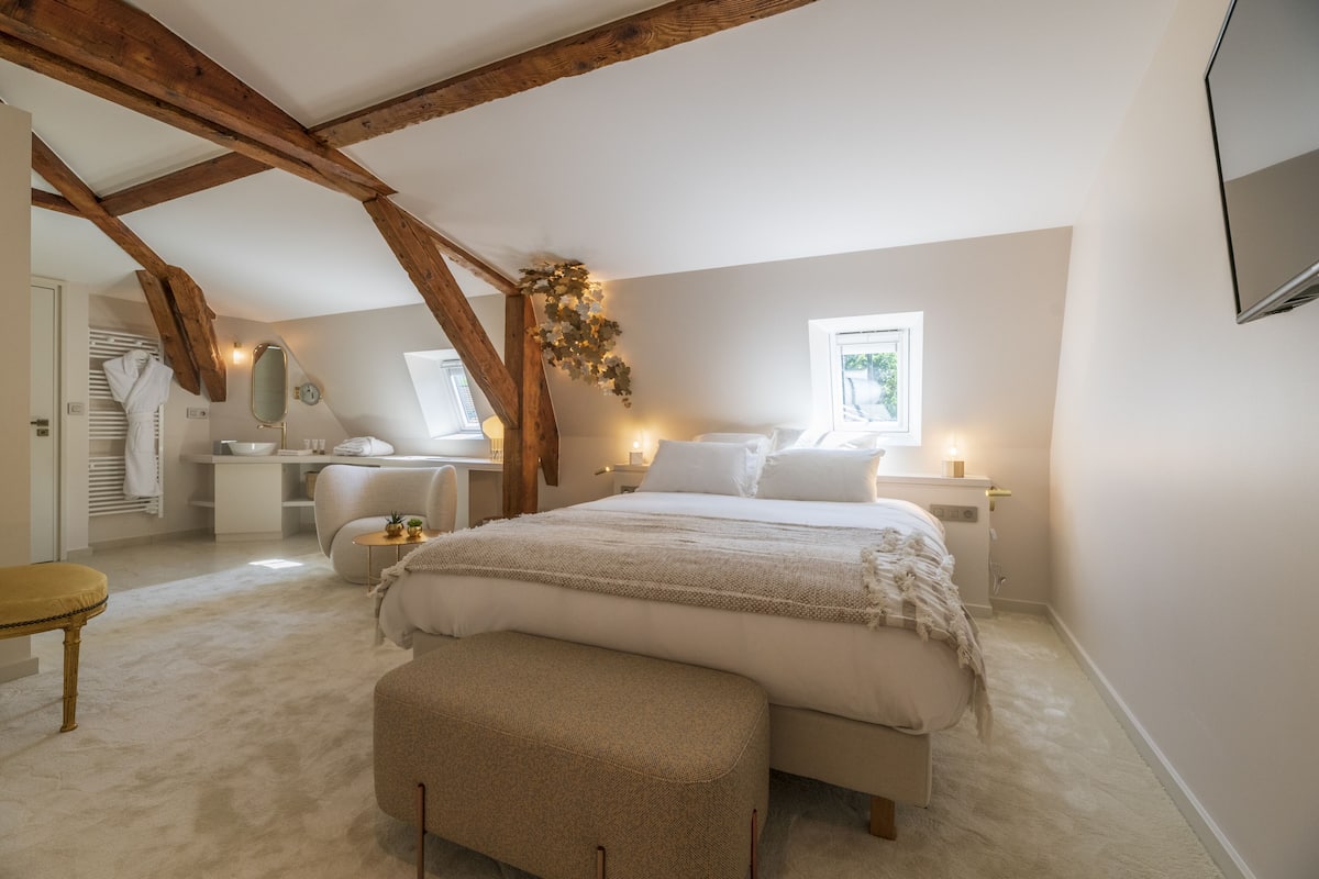 A bedroom with a large bed, a desk, a chair, and a window.