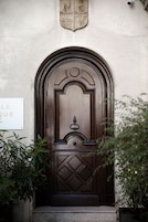 Una puerta de madera con un diseño decorativo, un letrero encima y plantas alrededor de la entrada.