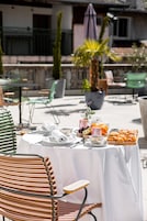 Un área de comedor al aire libre con una mesa dispuesta para dos personas, mostrando diversos alimentos y una pequeña planta decorativa.