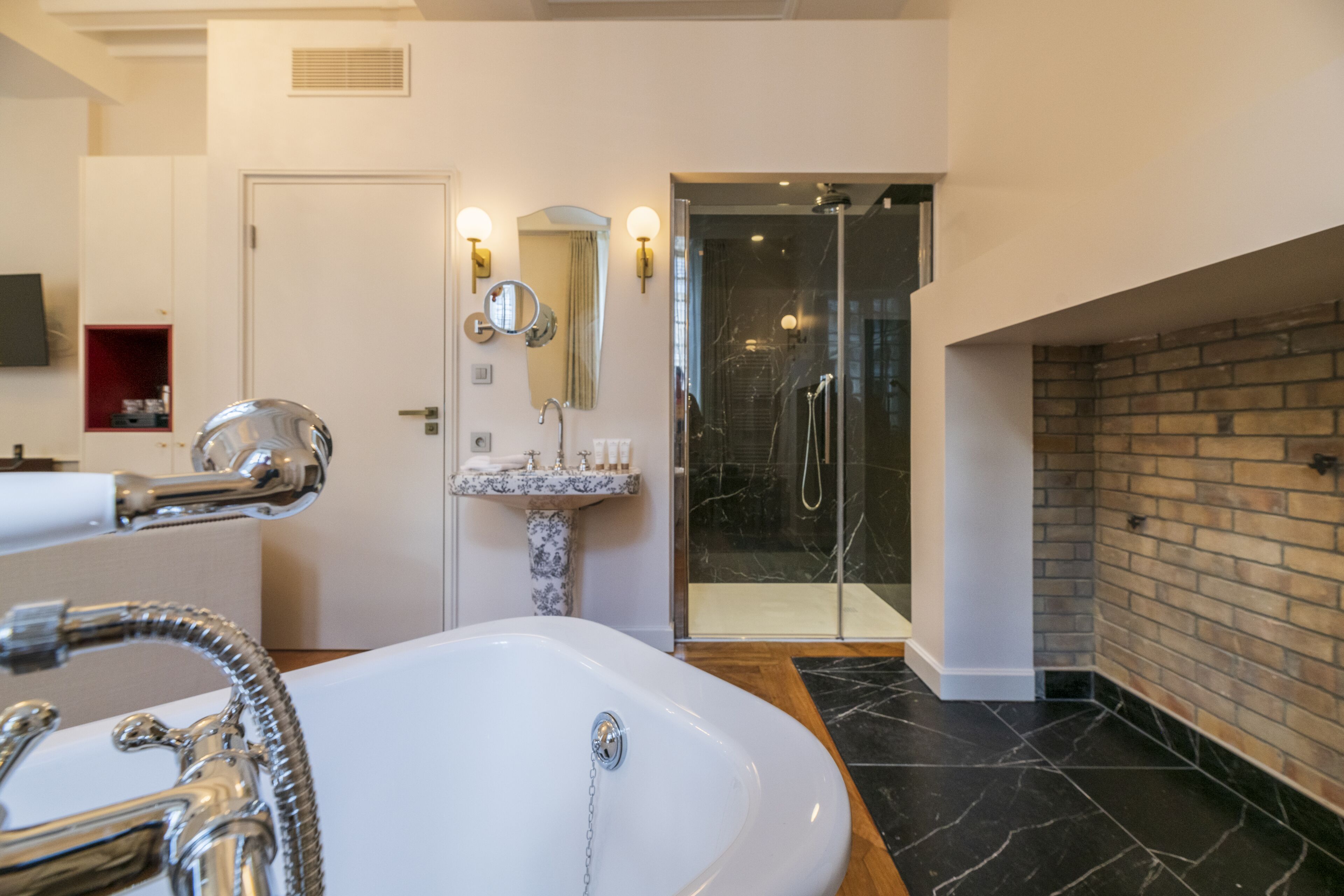 Un baño moderno con una bañera blanca grande, un lavamanos de mármol, una ducha con cerramiento de vidrio y una pared decorativa de ladrillo.