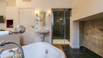 Un baño moderno con una bañera blanca grande, un lavamanos de mármol, una ducha con cerramiento de vidrio y una pared decorativa de ladrillo.