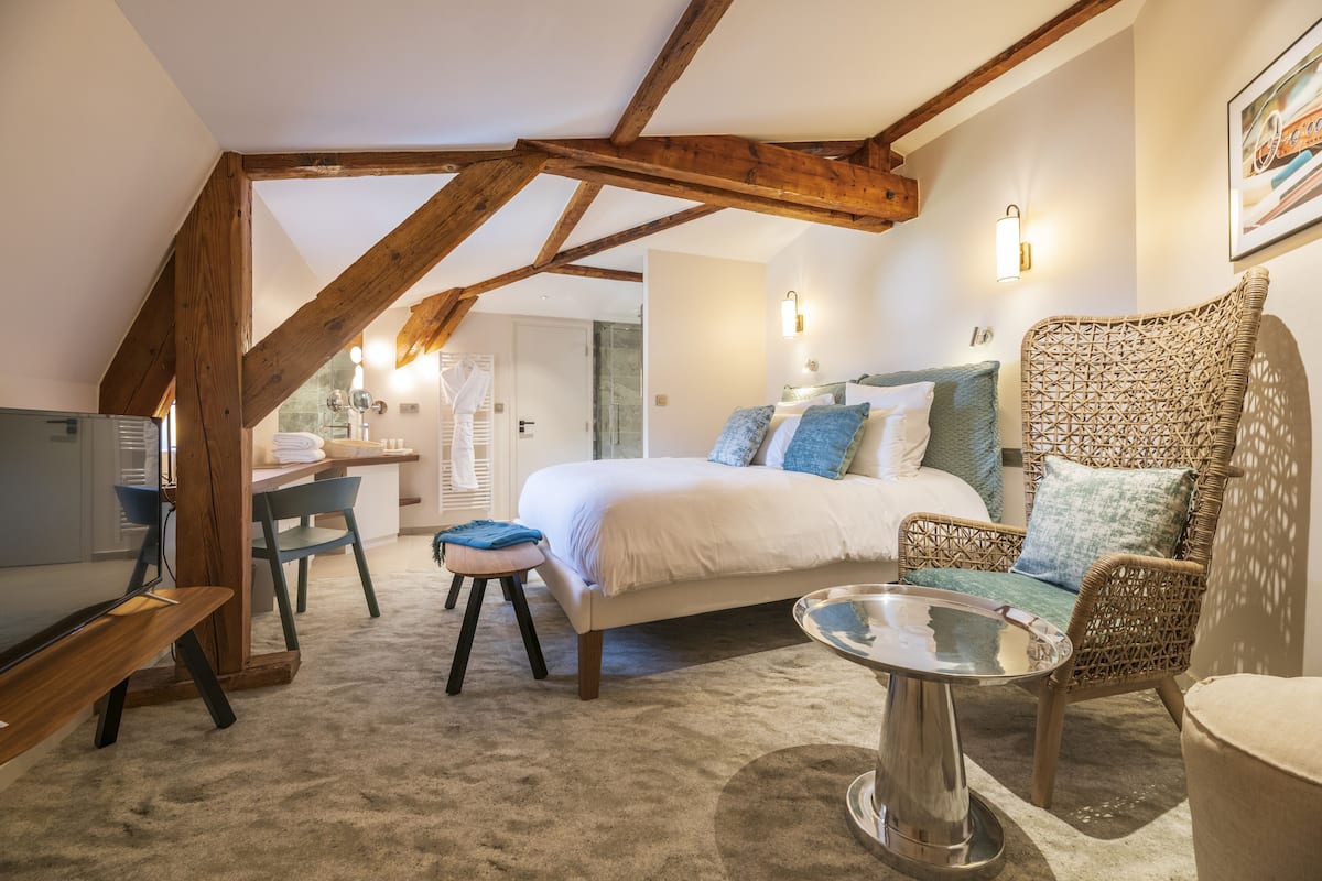 A bedroom with a bed, a wicker chair, a small table, and a desk with a chair.