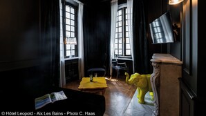 A dimly lit room with two large windows, a yellow table with a glass, a clear chair, and a yellow elephant sculpture.