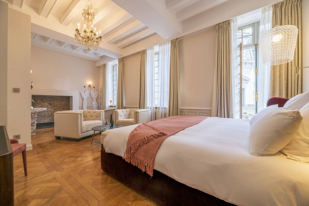 A spacious bedroom with a large bed, a fireplace, a seating area, and large windows.