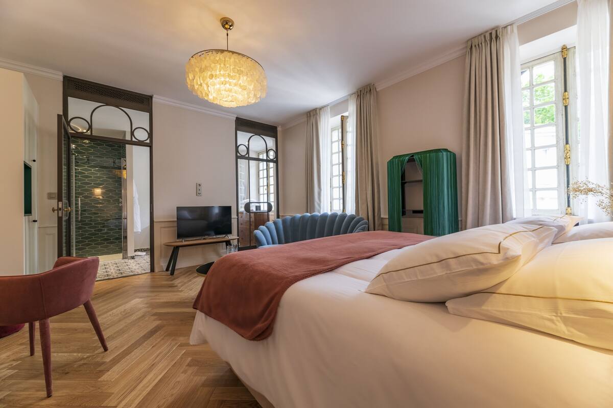 A hotel room with a large bed, a television, a seating area with a chair, and a view of the outdoors.