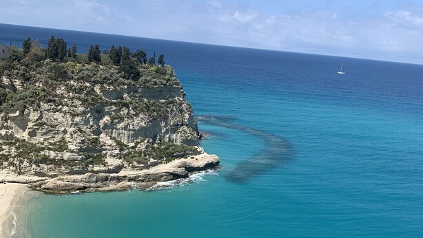 A coastal landscape with a clear beach, rocky cliffs, and a calm sea.