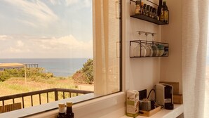 A kitchen with a view of the sea, a basket of fruit, and kitchen appliances.